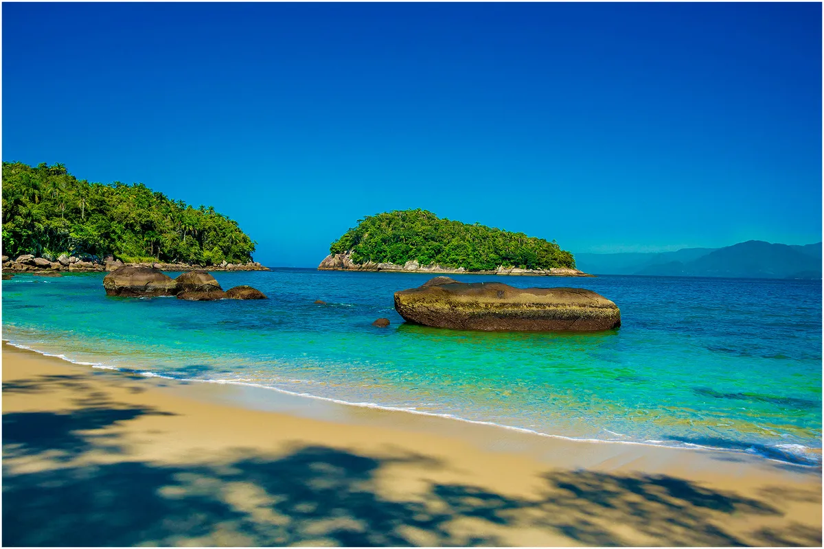 Praia da Ilha das Couves em Ubatuba com água cristalina, rochas e Mata Atlântica ao fundo