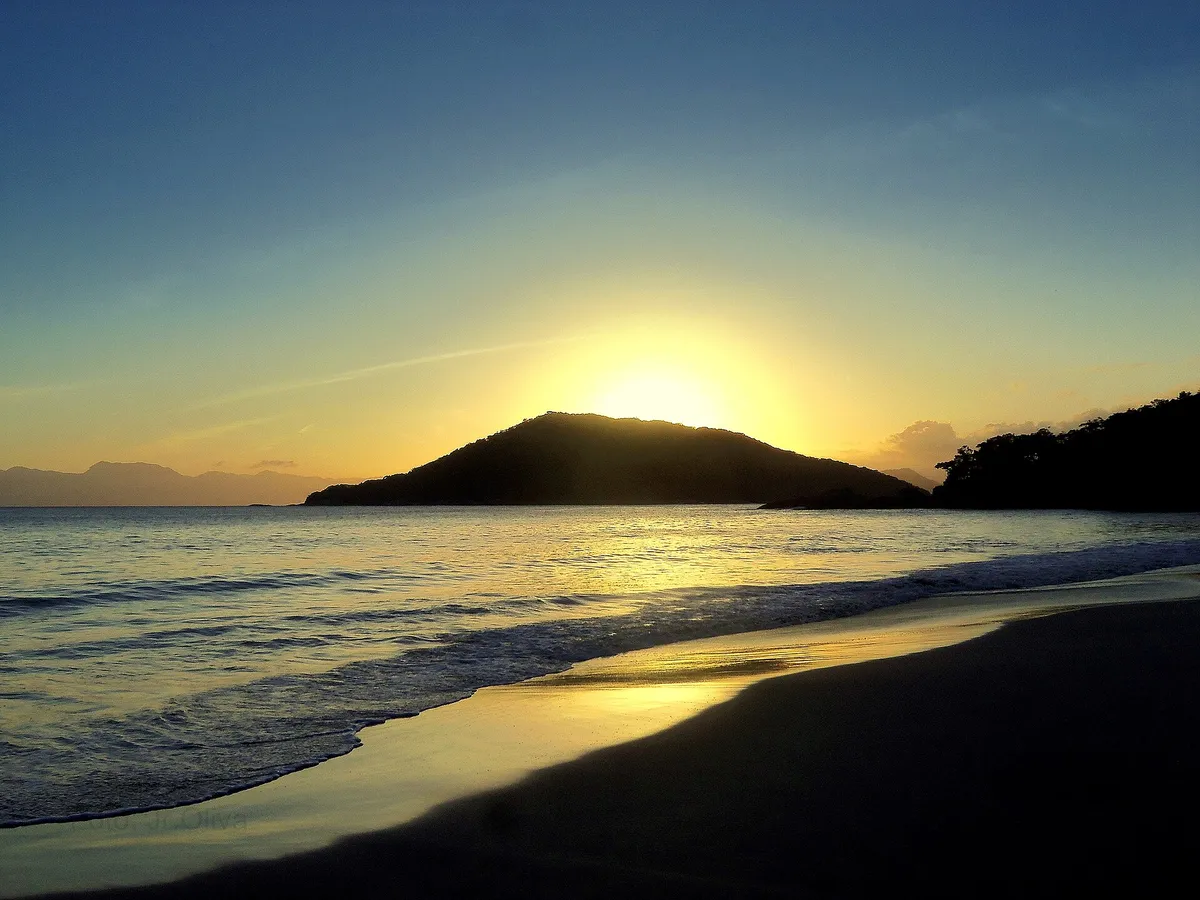 Pôr do sol na Praia do Itaguá, em Ubatuba, com o sol se pondo atrás do morro